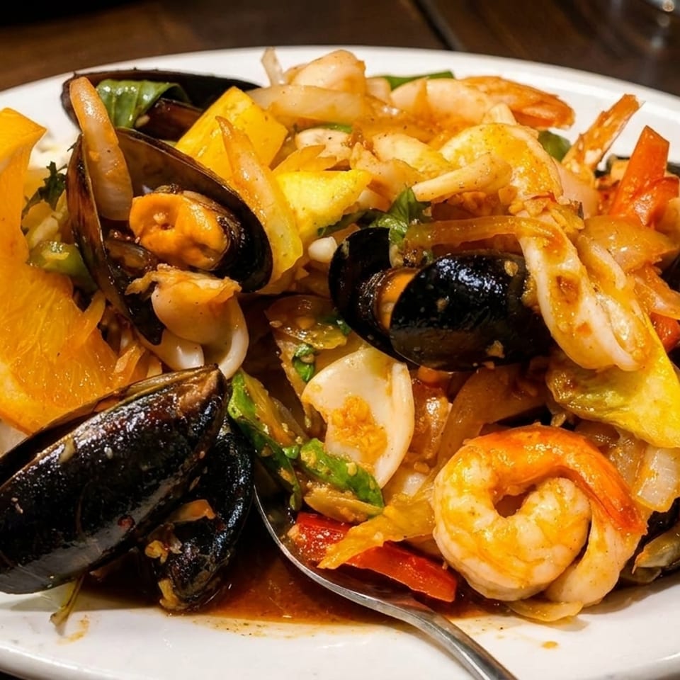 Seafood dish with mussels, shrimp, and mixed vegetables, garnished with an orange slice.