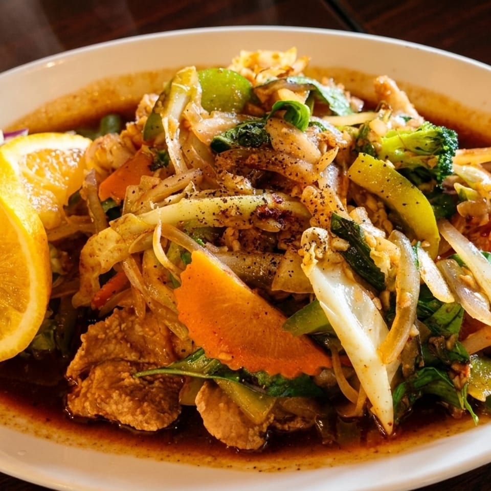 A stir-fried dish with mixed vegetables, a rich sauce, and an orange slice on a white plate.