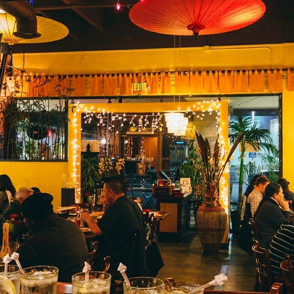 A bustling restaurant interior with patrons dining under warm lights and decorative umbrellas.