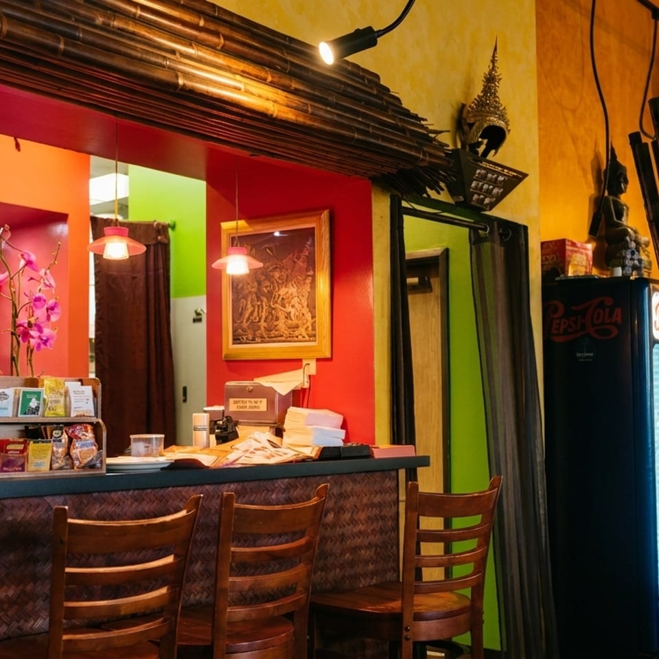 Vibrant restaurant interior featuring a bar, wooden stools, golden clock, and bamboo accents.